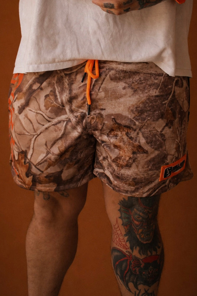 Person wearing camouflage shorts with orange drawstrings on a brown background
