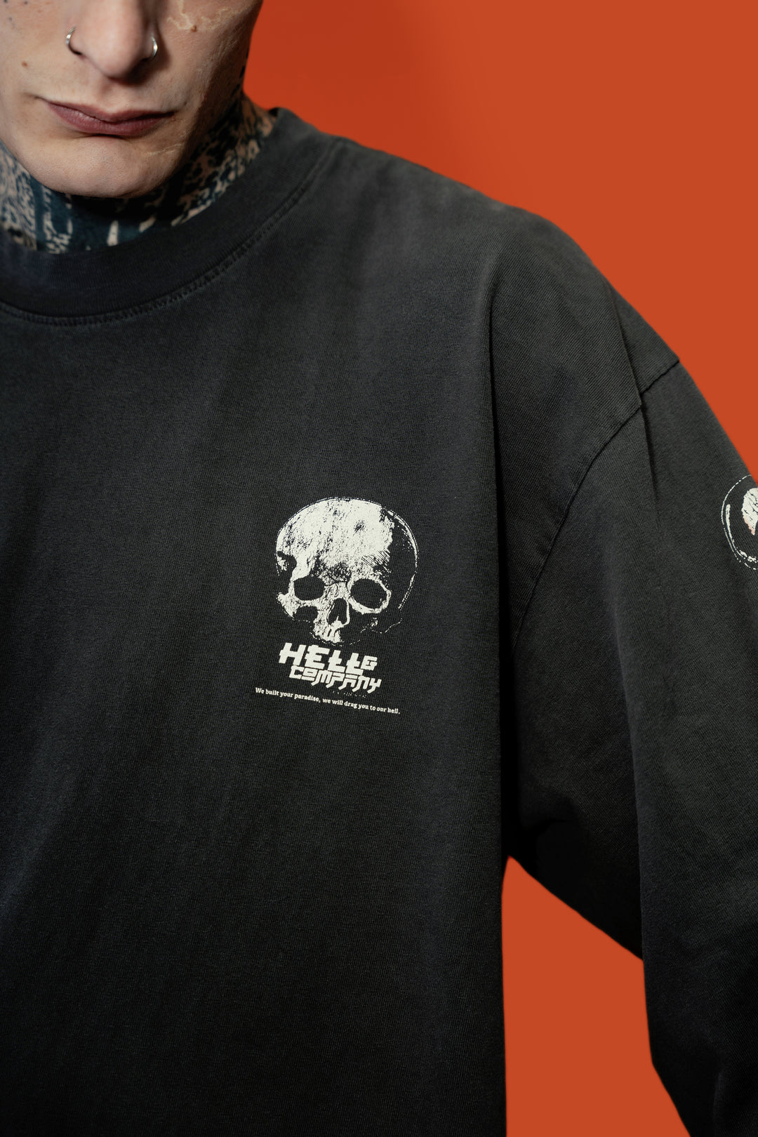 A close-up of a person wearing a faded black oversized crewneck sweatshirt with a distressed white skull and 'HEEEP COMPANY' text on the chest, set against a solid orange background.