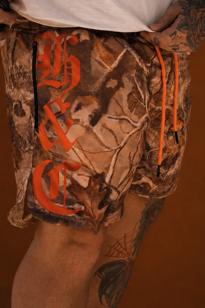 Camouflage shorts with orange drawstring and brand logo on a brown background