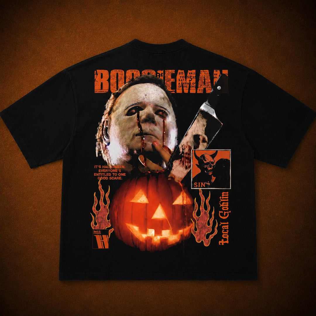 A black short-sleeve graphic T-shirt laid flat against a textured brown background. The shirt features a large front print with a horror-themed design: orange 'BOOSEMAN' text at the top, a pale face holding a knife above a glowing jack-o'-lantern, orange flames, and smaller graphic elements including a devil portrait and vertical 'Local Goth' text.