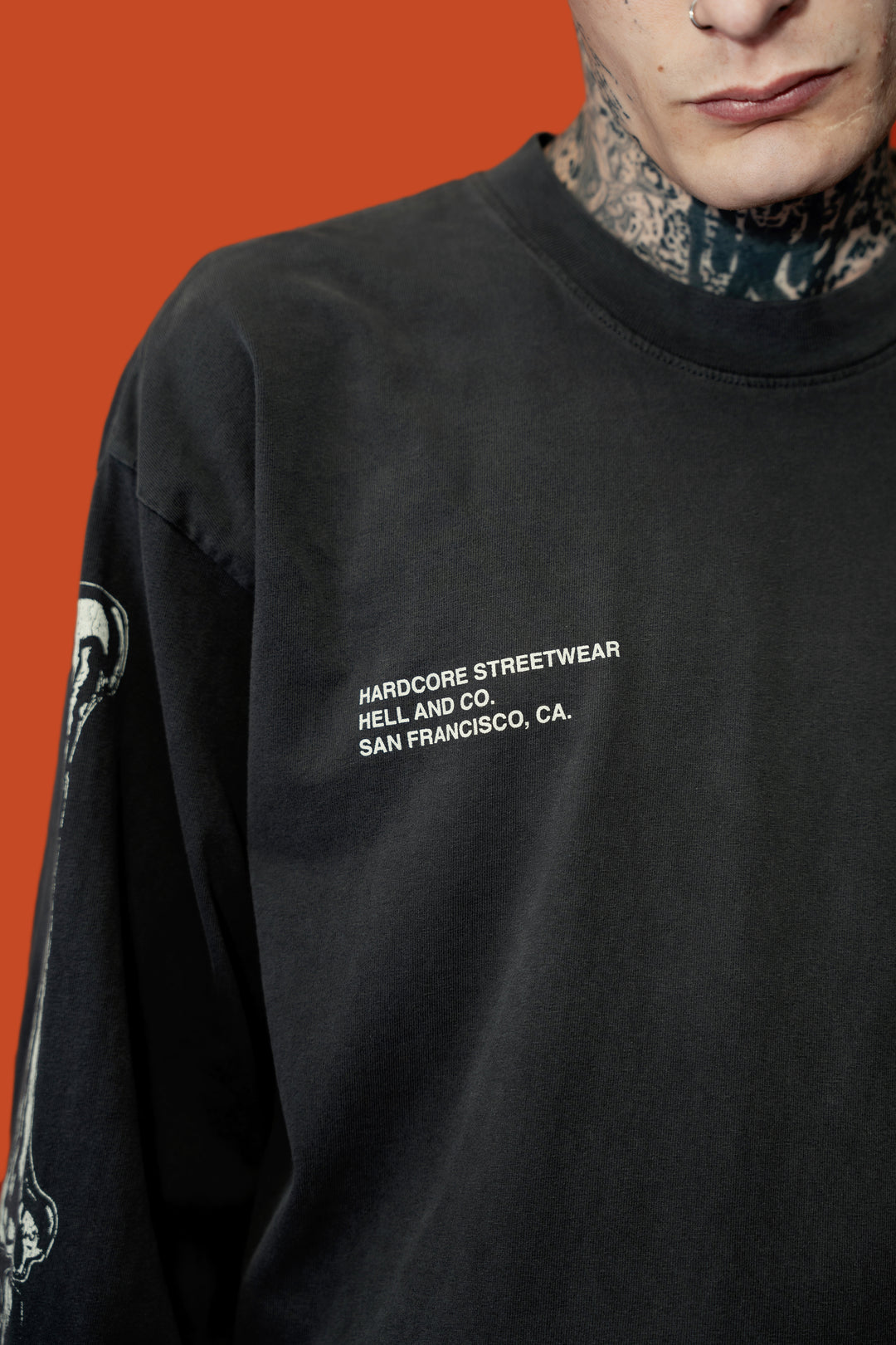 A close-up of a person wearing a black long-sleeve crewneck sweatshirt with white text on the chest reading 'HARDCORE STREETWEAR HELL AND CO. SAN FRANCISCO, CA.