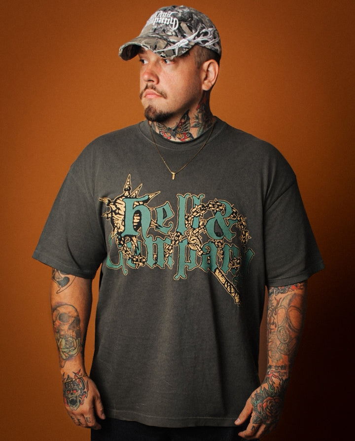 Man wearing a dark gray t-shirt with a graphic design and camouflage cap against an orange background