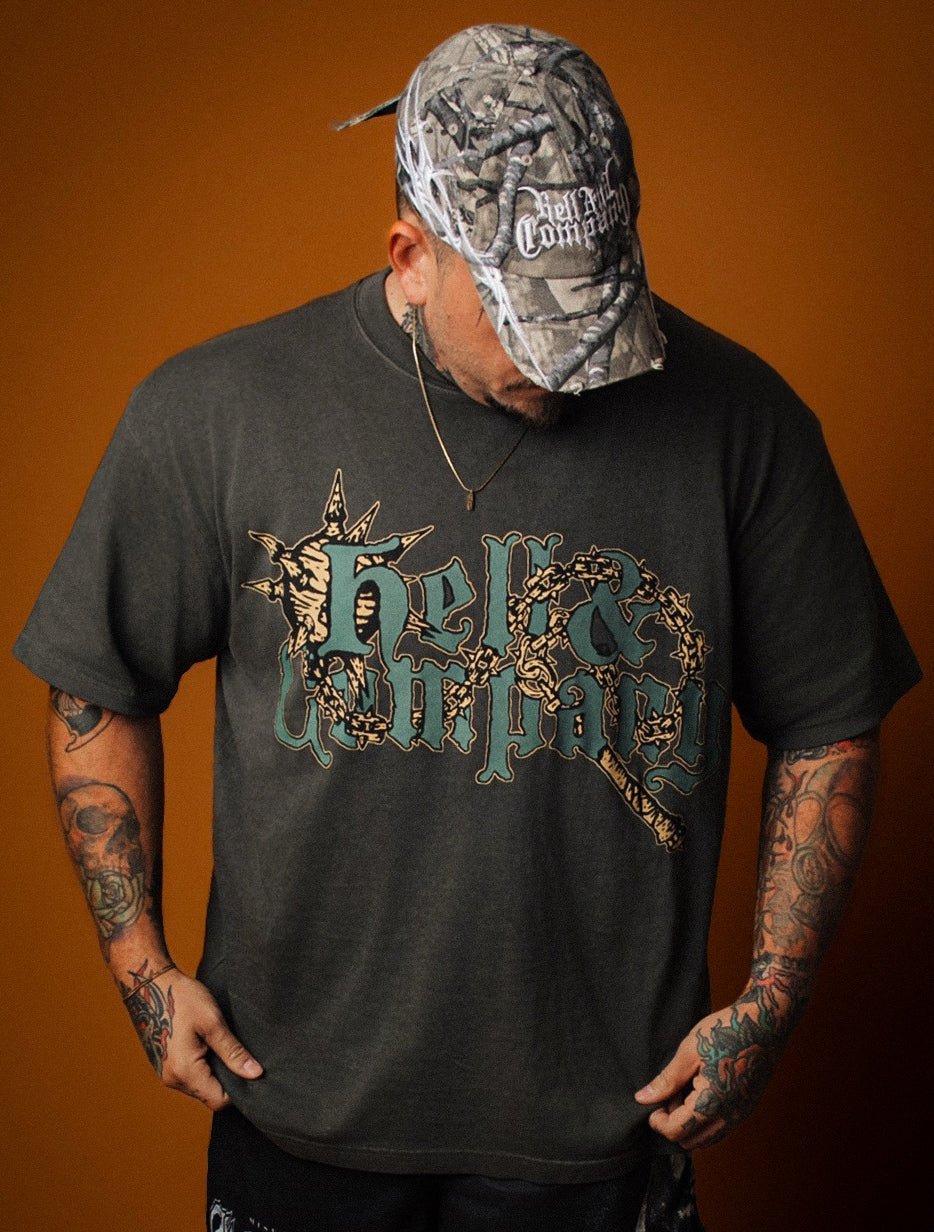 Person wearing a black t-shirt with a graphic design and a camouflage cap against an orange background