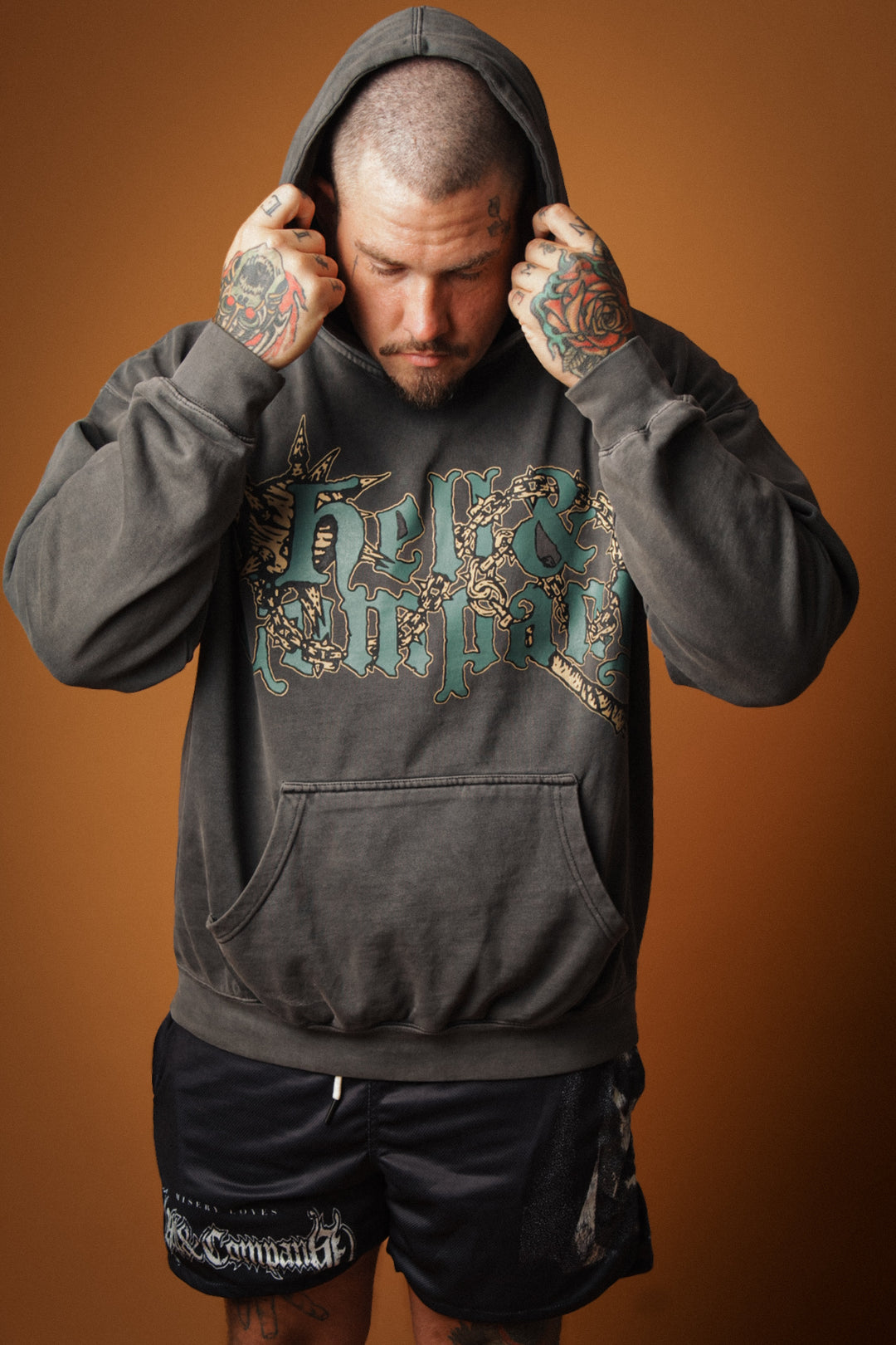 Man wearing a dark gray hoodie with graphic design on a brown background