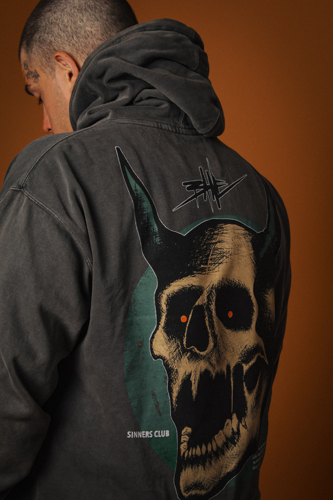 Person wearing a dark jacket with a skull design on the back against an orange background