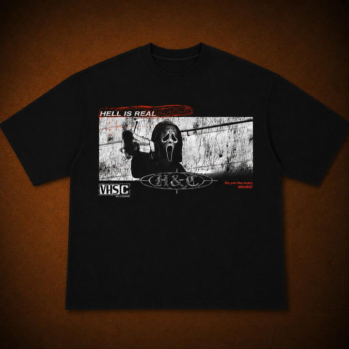 A black short-sleeve graphic t-shirt laid flat against a textured brown background. The front of the shirt features a rectangular horror-themed print with a Ghostface silhouette, the text 'HELL IS REAL', 'VISC', and 'Do you like turningbranded meat?', along with a stylized 'H&C' logo.